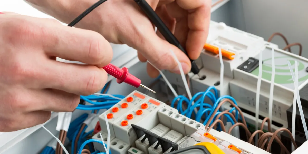 Close-up of hands wiring an electrical circuit board.