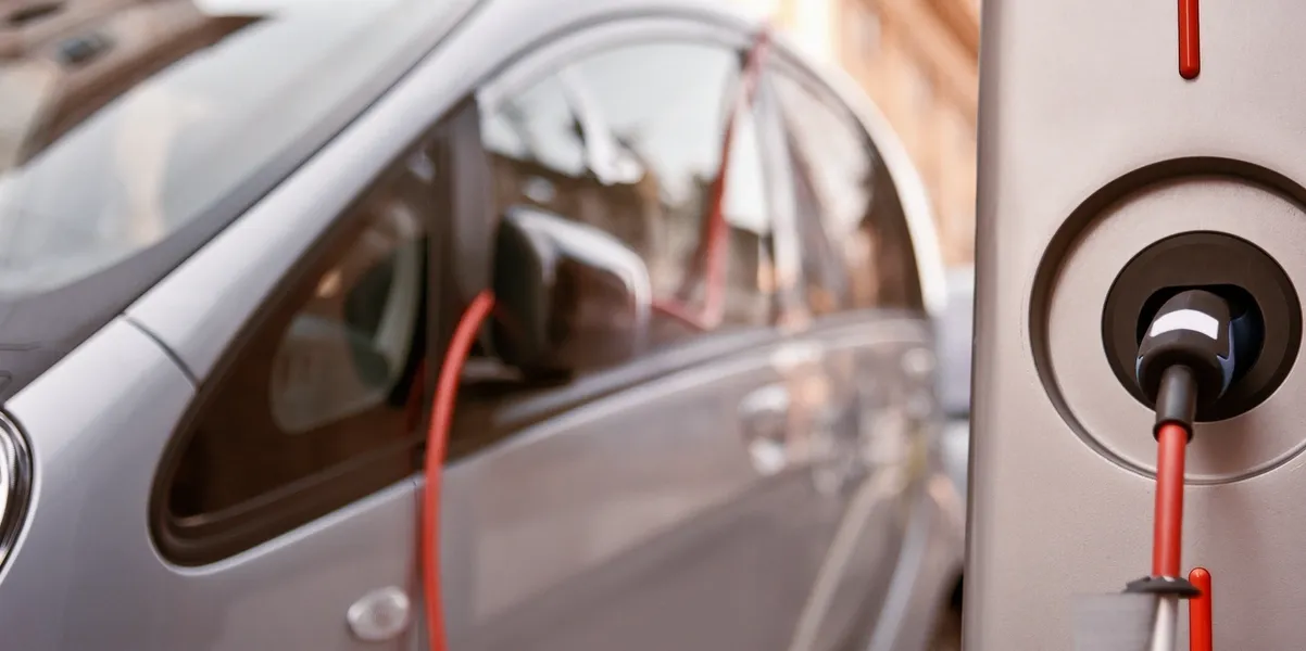 Electric car charging with a red cable connected to its side.